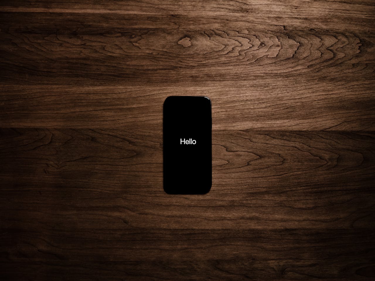 A smartphone displays 'Hello' against a dark wooden background, offering a sleek tech aesthetic.