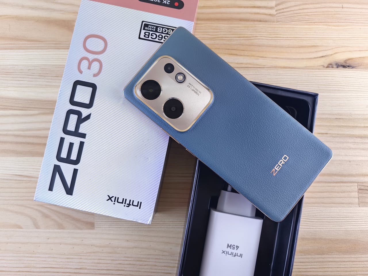 Infinix Zero 30 smartphone with original packaging and accessories on a wooden surface.