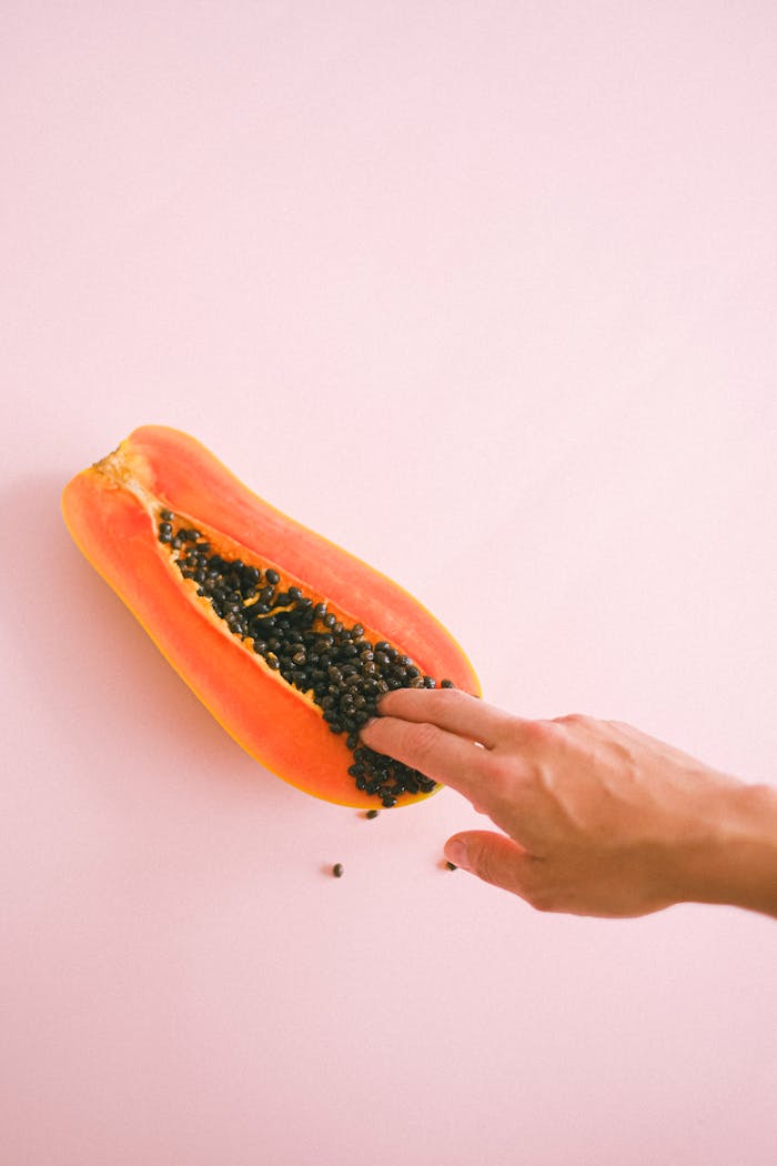 Aesthetic composition of a papaya and hand on soft pink backdrop, offering a sensual visual experience.